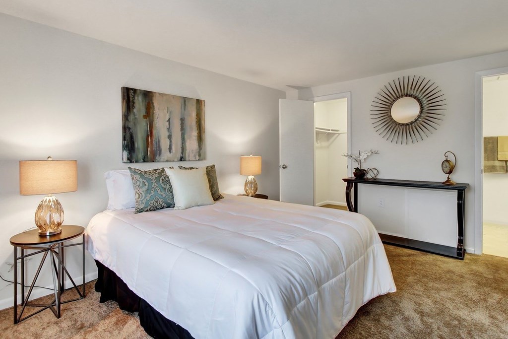 A bedroom with a large bed, two lamps, and a painting on the wall.