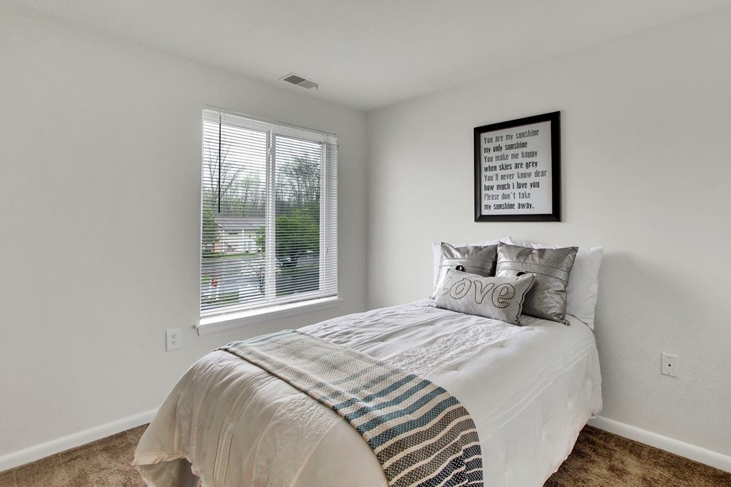 A bedroom with a bed, pillows, and a framed quote on the wall.