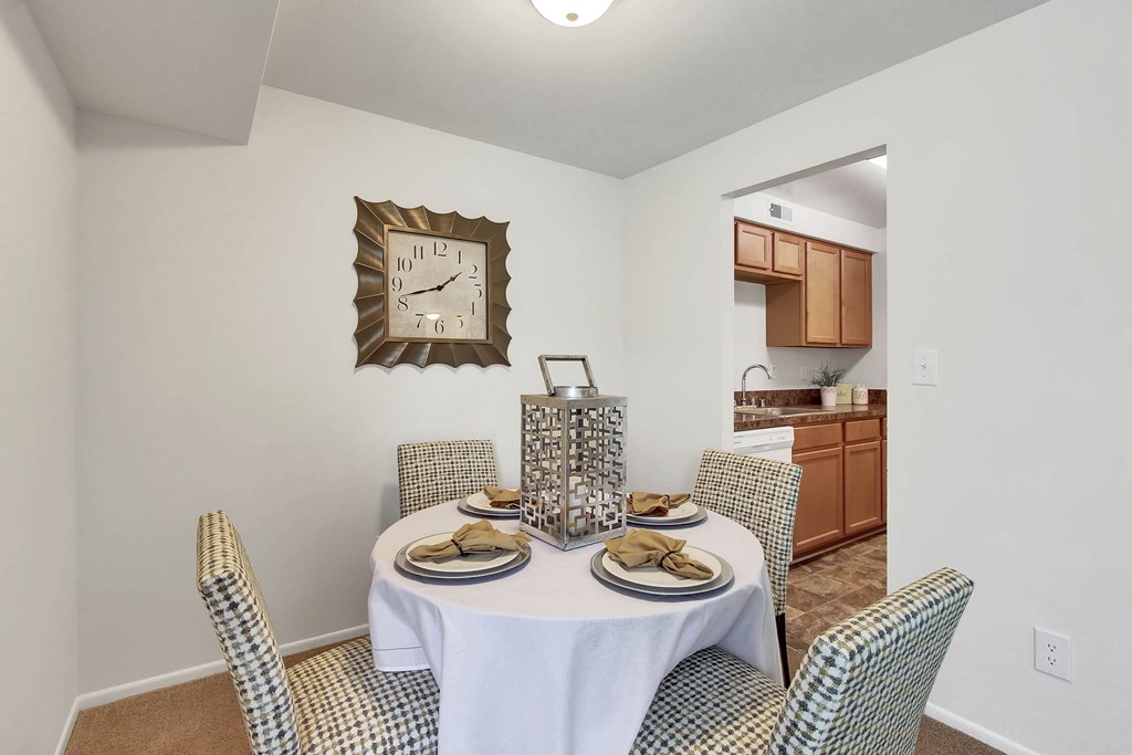 A dining room with a table set for two and a clock on the wall.