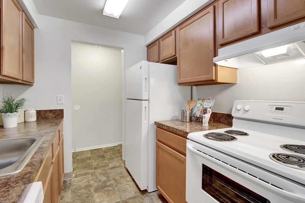 A kitchen with a white refrigerator, white stove, and brown cabinets.