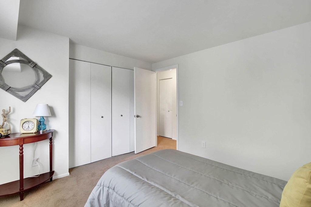 A bedroom with a bed, a nightstand with a clock, a lamp, and a wall-mounted mirror.