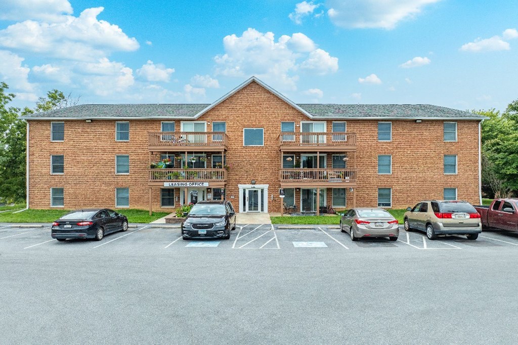 A parking lot in front of a brick building with cars parked.