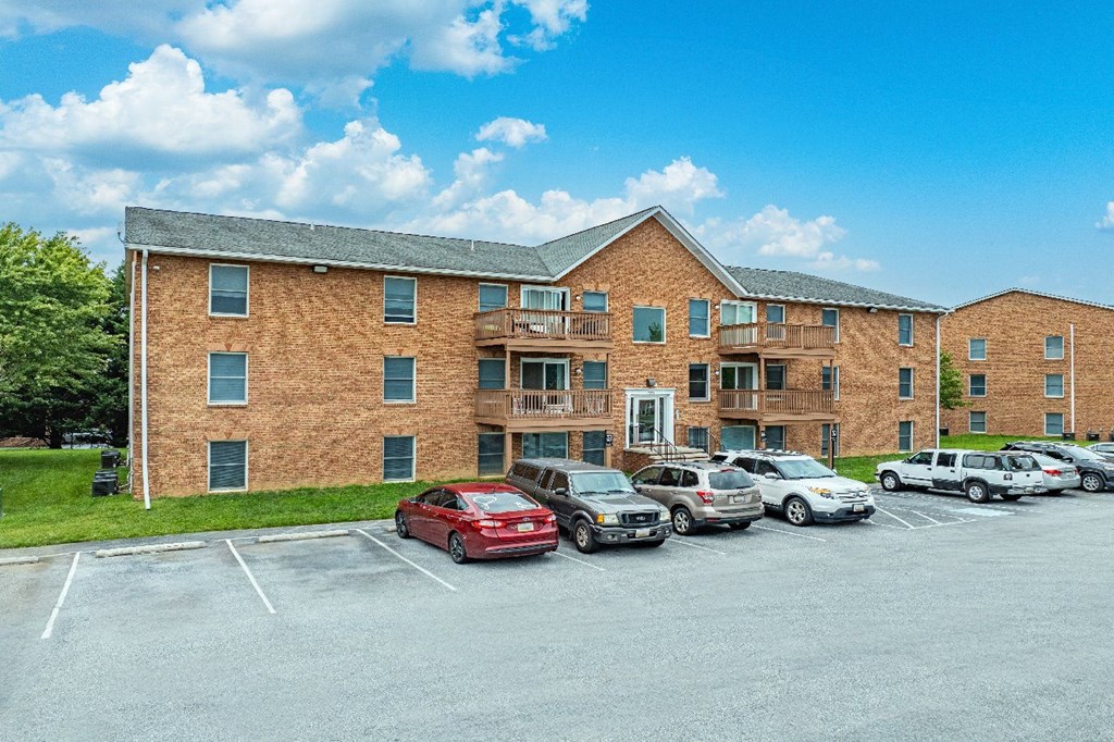 A red car is parked in a parking lot in front of a brick building.