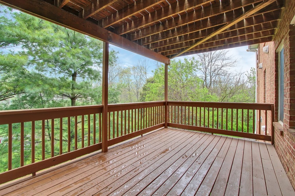 A wooden deck with a railing and a roof overlooking a wooded area.