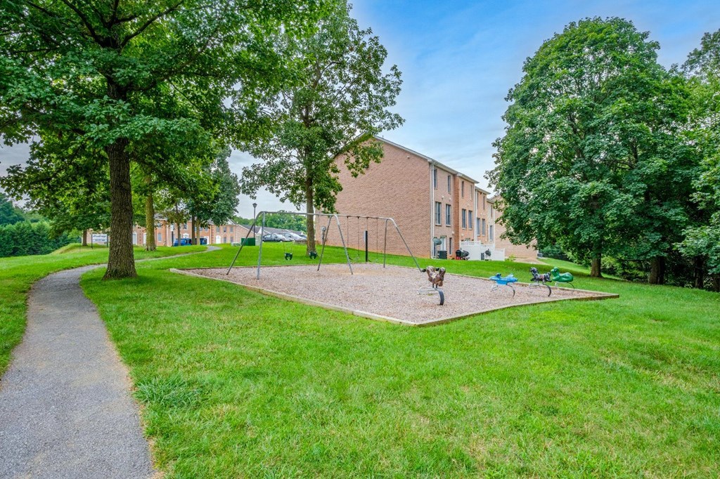 A playground with a slide and swings is surrounded by a grassy area and trees.