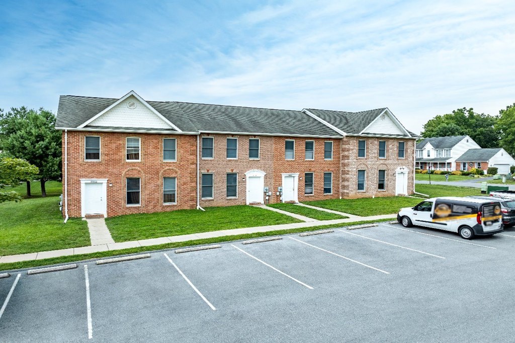 A parking lot in front of a brick building with a white van parked.