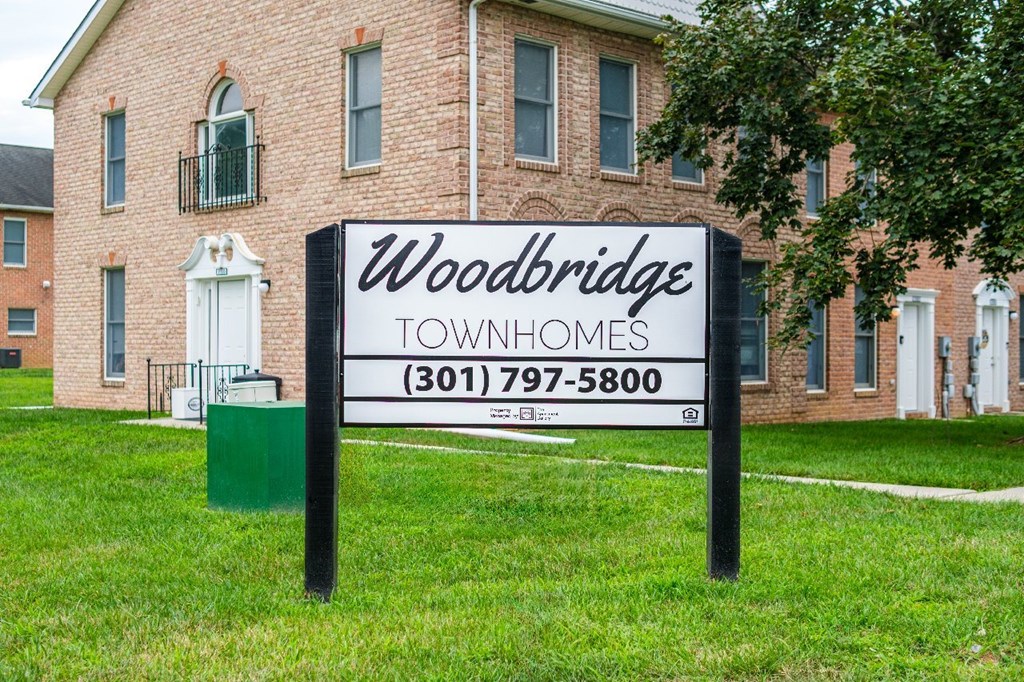 A sign for Woodbridge Townhomes stands in front of a brick building.