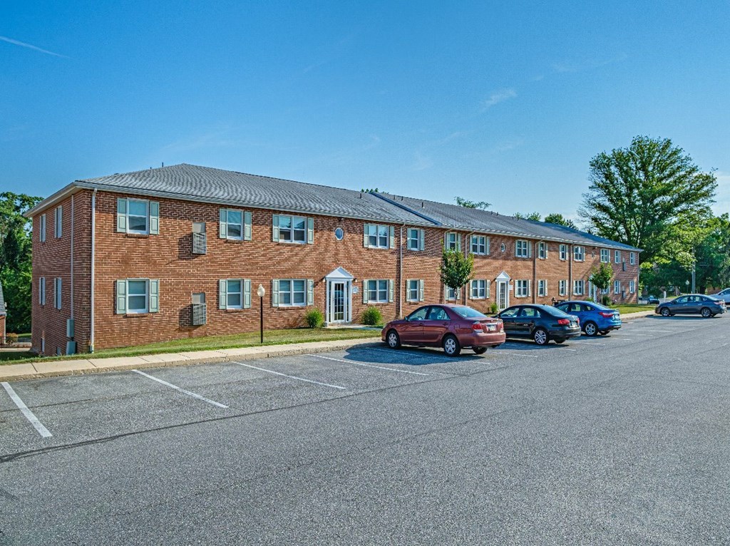A red car is parked in a parking lot in front of a brick building.