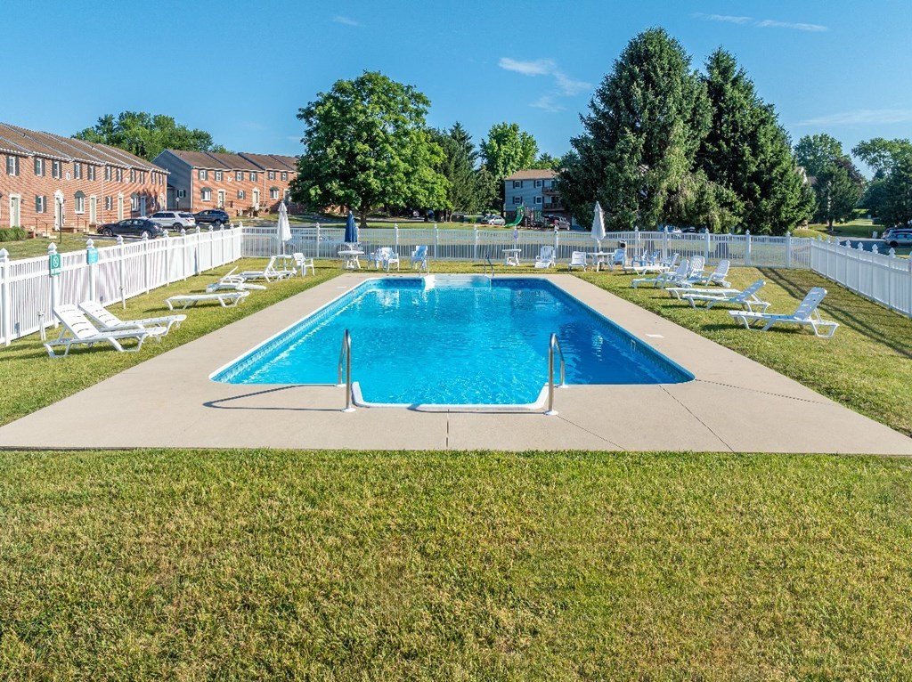 A large swimming pool surrounded by lawn chairs and a white fence.
