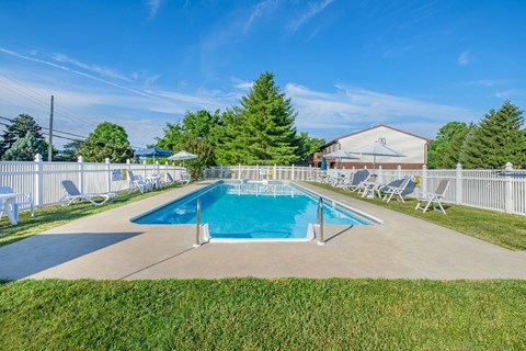 A pool surrounded by lawn chairs and a white fence.