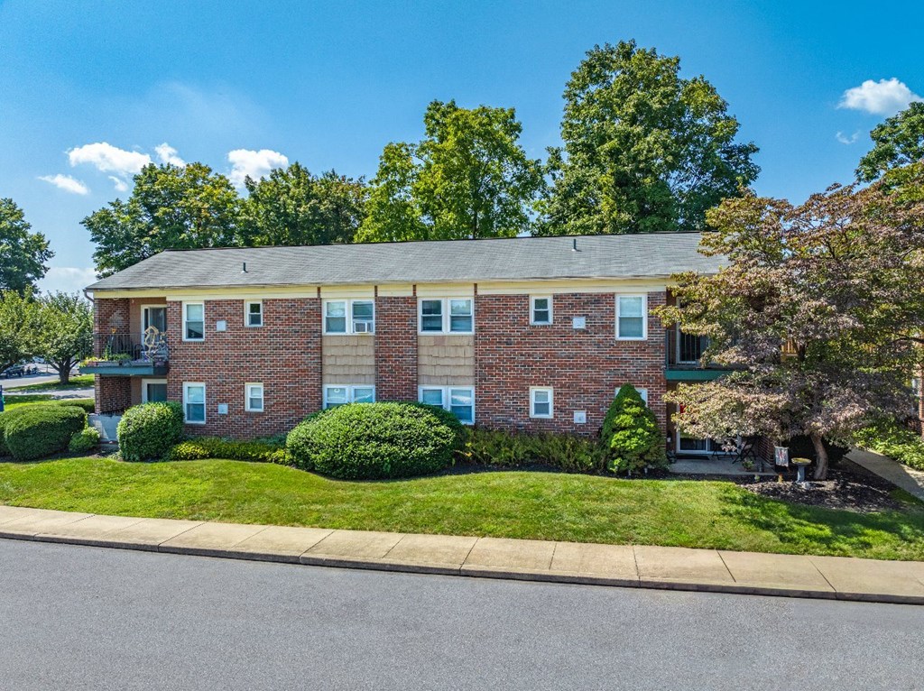 A red brick apartment building with green bushes in front.