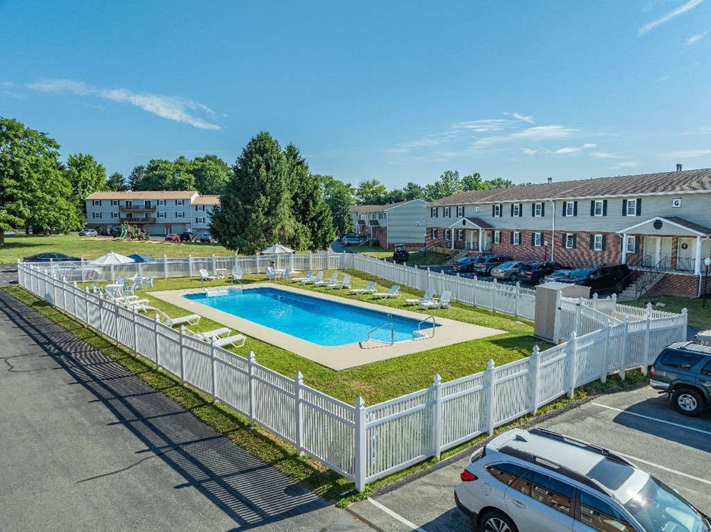 A white fence surrounds a swimming pool in a sunny day.
