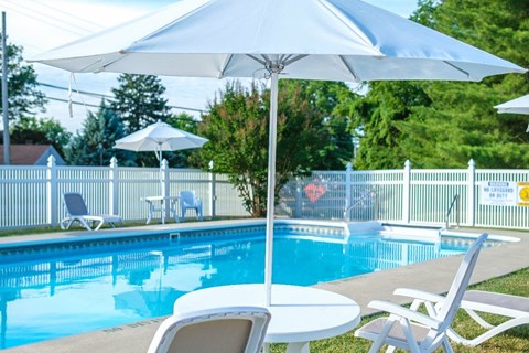 A pool with a white umbrella and chairs around it.