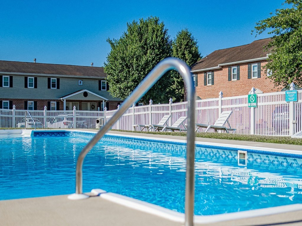 A swimming pool with a metal ladder in the foreground and a building in the background.