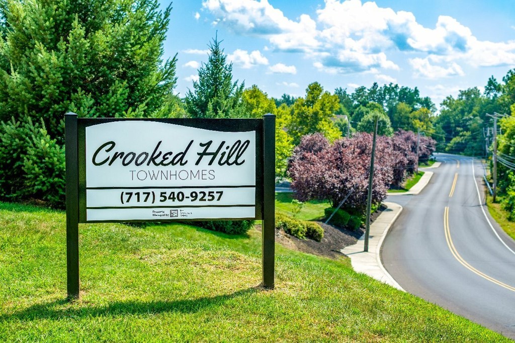 A sign for Crooked Hill Townhomes stands in front of a tree-lined street.