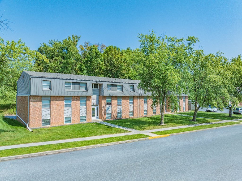 A modern building with a grey roof and red brick walls is surrounded by green trees.