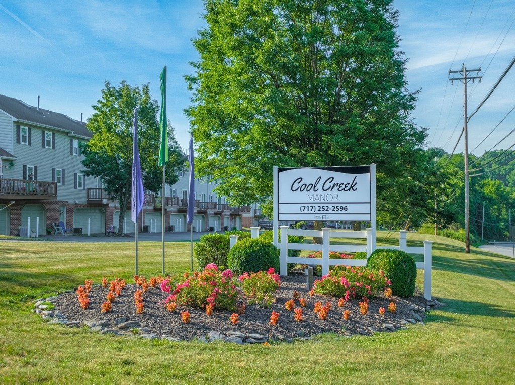 A sign for Cool Creek Manor with a flower bed in front.