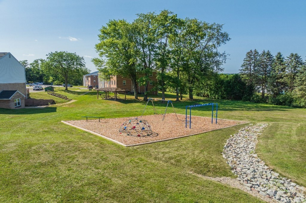 A playground with a swing set and a sandbox in the middle of a grassy area.