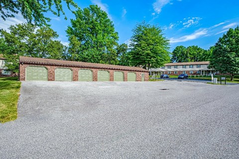 A long building with a red brick wall and a parking lot in front.