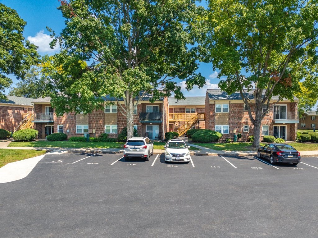 A parking lot in front of a brick building with cars parked.