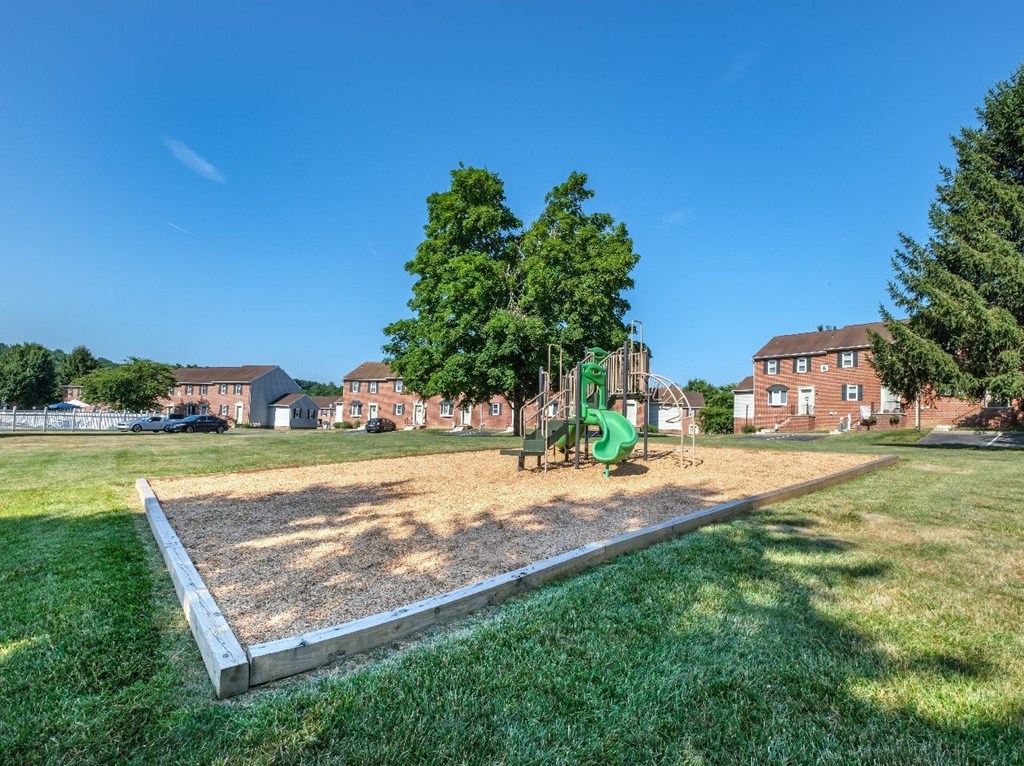 A playground with a green slide and a sandbox in the foreground.