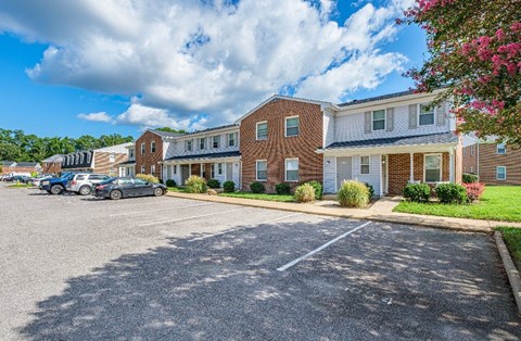 A parking lot in front of a brick building with cars parked.