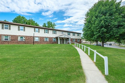 A grassy area in front of a building with a white fence.