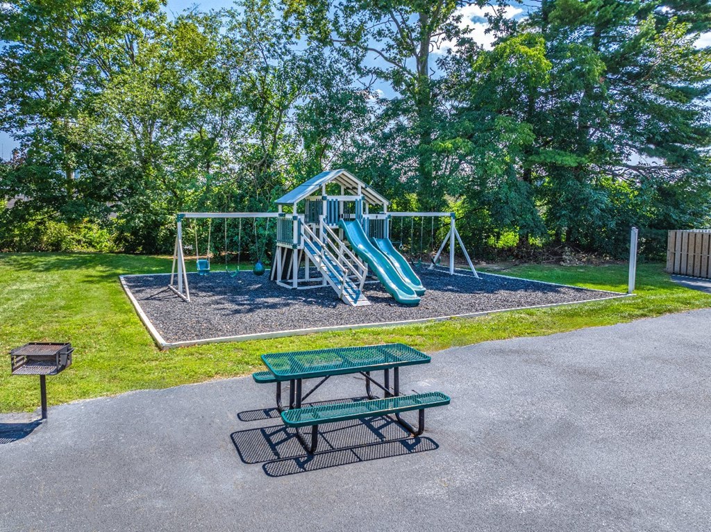 A playground with a green slide and picnic table.