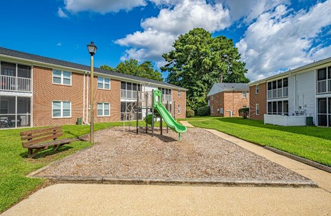 A playground area with a green slide in front of apartment buildings.