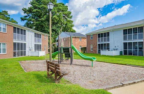 A playground with a green slide and a wooden bench in the foreground.