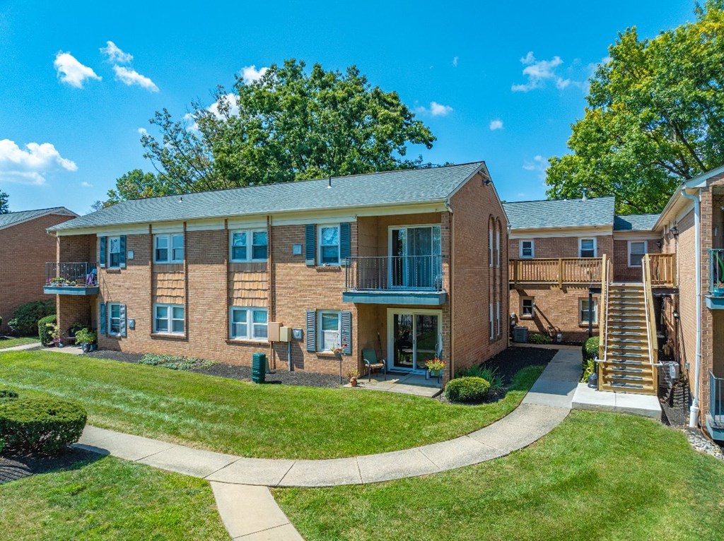 A sunny day at a brick apartment complex with green lawns and trees.