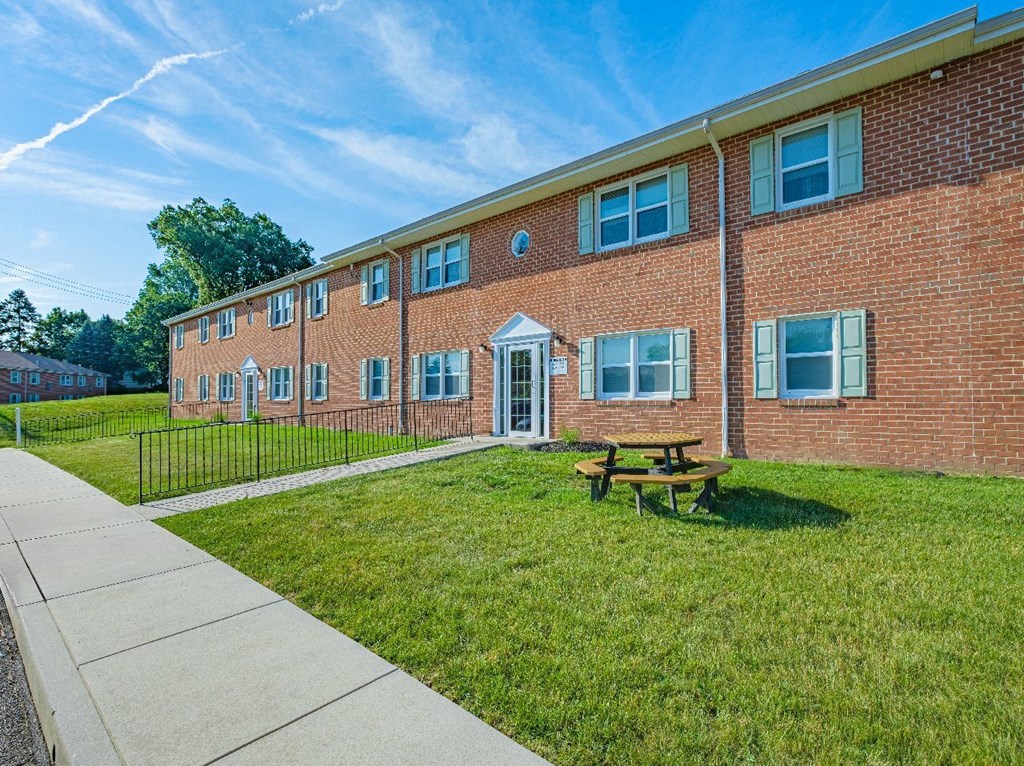 A red brick building with a white door and windows, a picnic table, and a black fence.