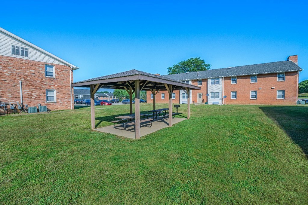A covered picnic area sits in the middle of a grassy field.