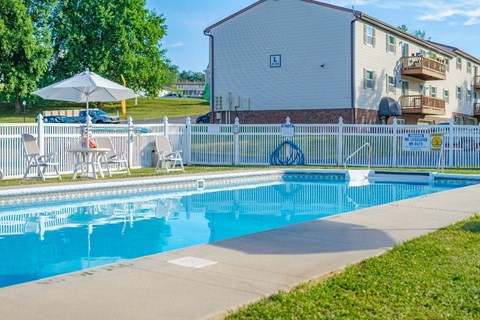 A pool surrounded by a white fence and chairs.