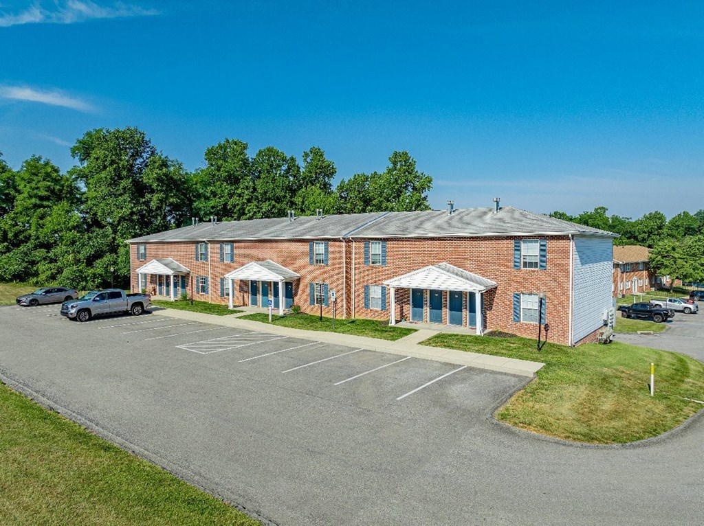 A parking lot in front of a brick building with a car parked in the lot.