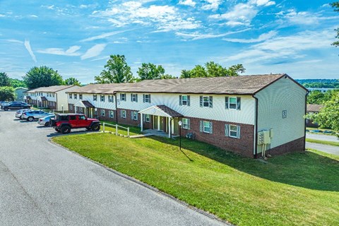 A red car is parked in front of a white building with a green lawn.