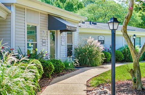 A house with a white exterior and a black awning is surrounded by greenery.