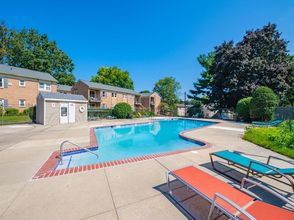 A swimming pool surrounded by a concrete patio and lounge chairs.