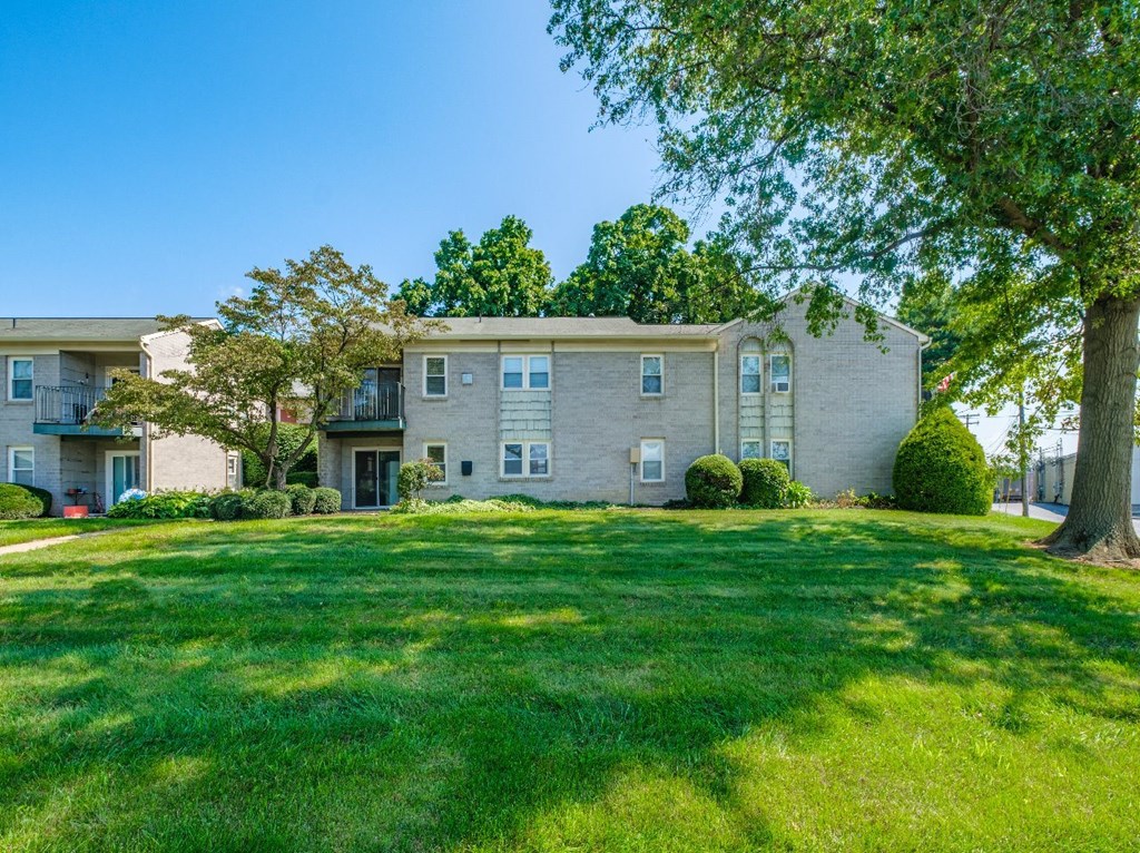 A large grassy area in front of a two-story building with a tree in the front yard.