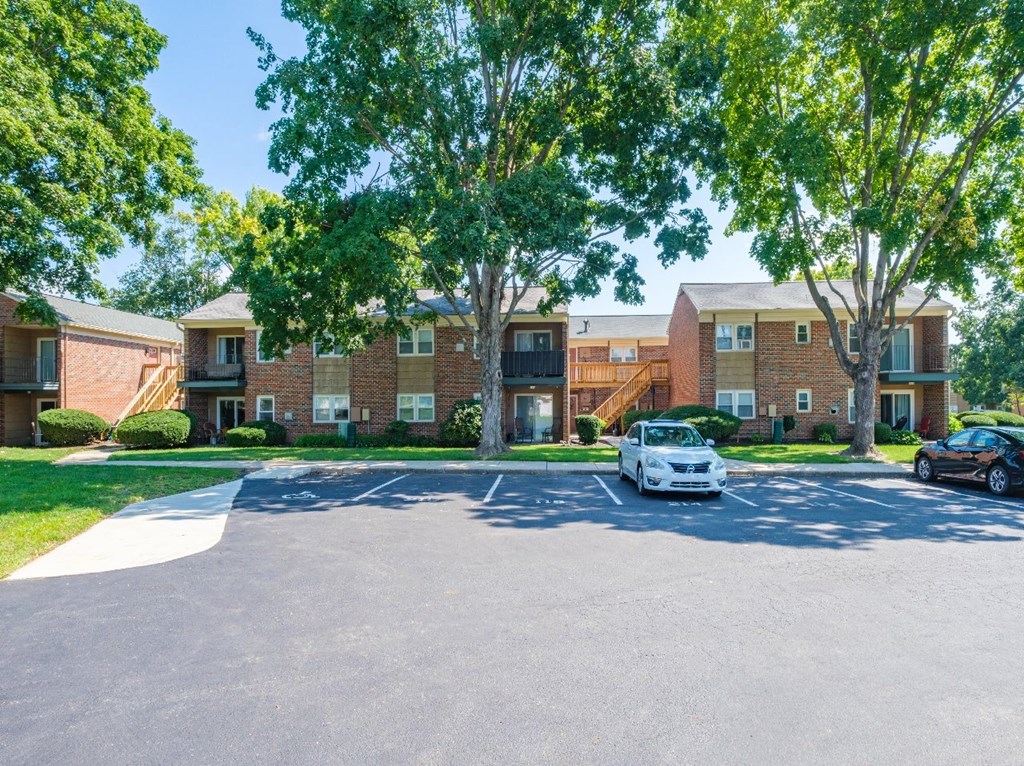 A white car is parked in a parking lot in front of a brick building.