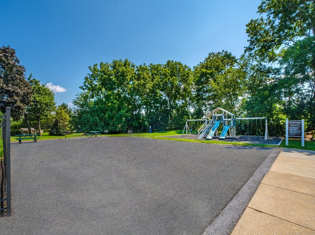 A playground with a slide and a signboard is surrounded by trees.