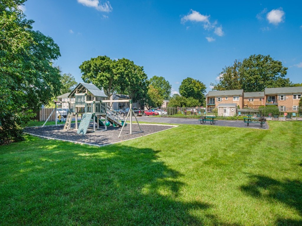 A playground with a green slide and a play area surrounded by a grassy field.