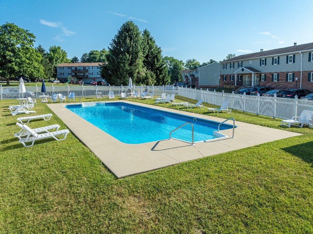 A swimming pool surrounded by lawn chairs and a white fence.