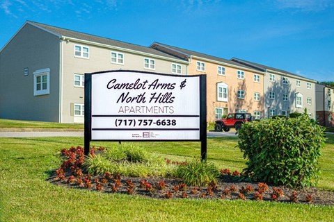 A sign for Camelot Arms North Hills Apartments with a phone number on it.