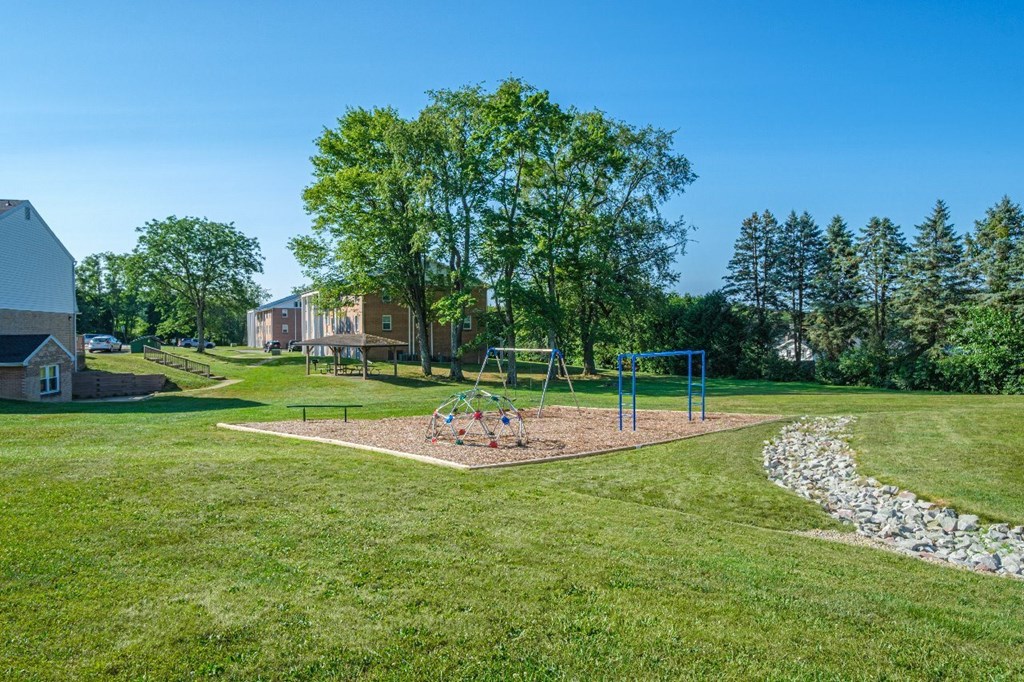 A playground with a swing set and a baseball diamond in the middle of a grassy area.