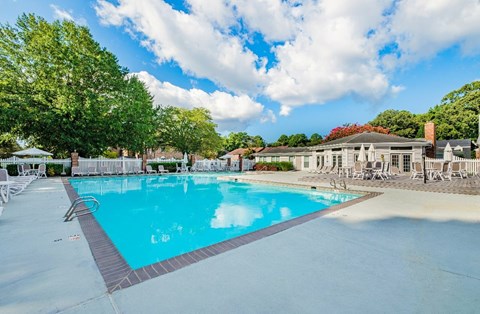 A large swimming pool surrounded by trees and a building in the background.
