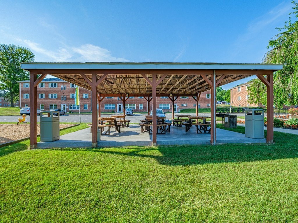 A covered picnic area with benches and a playground in the background.