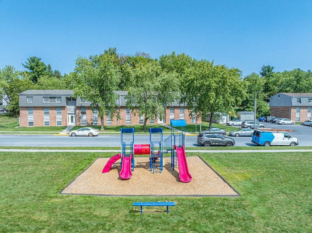 A playground with a red slide and a blue bench in the foreground.