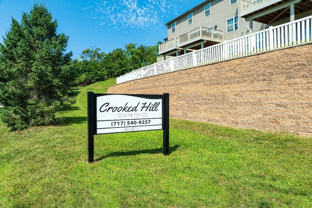 A sign for Crooked Hill Owned by Ownvoices stands in a grassy area.