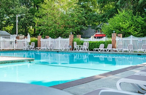 A pool surrounded by white chairs and a white fence.